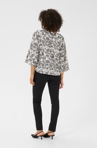 Haut à imprimé floral noir et blanc avec des manches trois-quarts, porté avec un jean skinny noir et des chaussures à talons slingback noires.