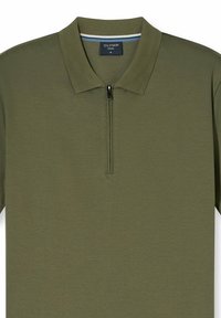 Olivgrünes Polohemd mit Reißverschlusskragen, aus weichem Stoff gefertigt. Es hat eine strukturierte Oberfläche und ein gestreiftes Band im Inneren des Kragens.