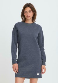 Robe-sweat à manches longues, de couleur bleu marine, en tissu doux, avec des poignets et un ourlet côtelés, et une petite étiquette de marque sur le bas du devant.