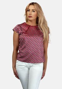 T-shirt z krótkim rękawem w geometryczny wzór w czerwono-czarnych odcieniach, z okrągłym dekoltem i luźnym krojem, zestawiony z białymi dopasowanymi spodniami.