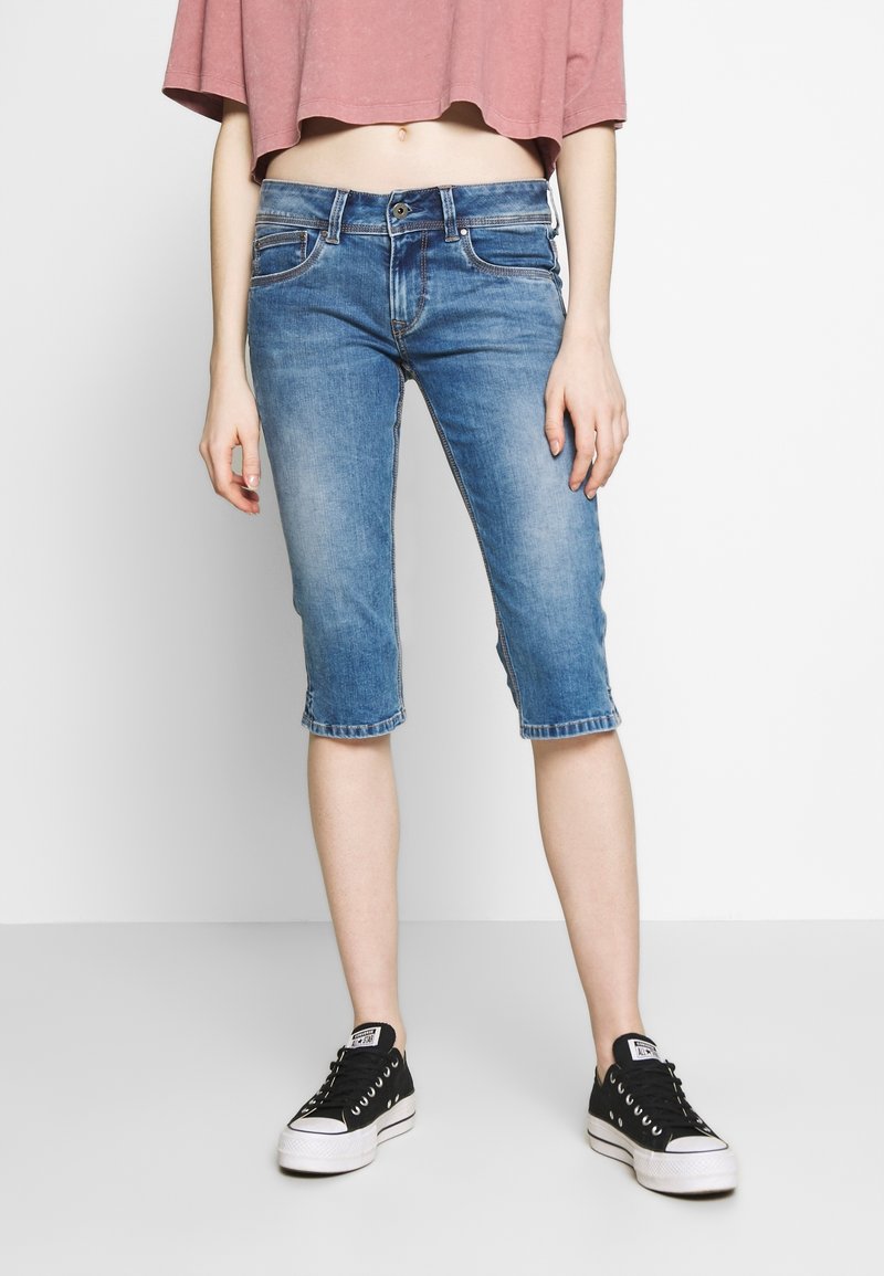 Pantalones capri de mezclilla en azul claro, con un corte holgado, dobladillos enrollados y un estilo clásico de cinco bolsillos, combinados con zapatillas negras.