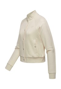 Veste bomber de couleur crème, à manches longues, avec boutons-pression, col, poignets et taille côtelés, et un petit logo sur la poitrine à gauche.