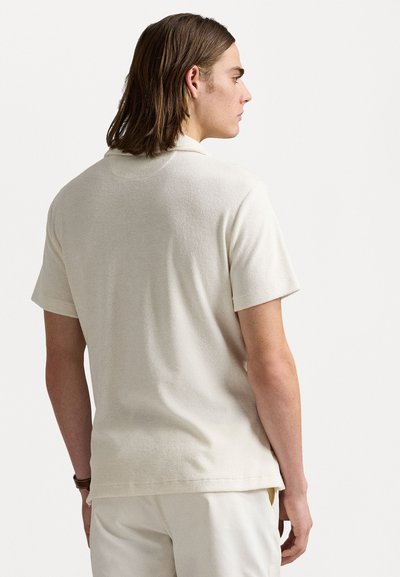 Bežna polo majica s kratkimi rokavi z mehkimi teksturami, ki ima klasičen ovratnik, šivani rob in sproščen kroj. Minimalističen dizajn.