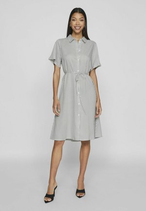 Páskované košilové šaty v šedé a bílé barvě, s krátkými rukávy, staženým pasem a sukní po kolena, v kombinaci s černými sandály na otevřené špičce.