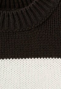 Jersey de punto con un cuello acanalado de color marrón oscuro y un cuerpo blanco en contraste, con una textura suave y un patrón de costura visible.