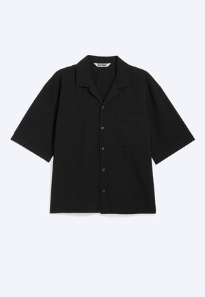 Chemise noire à manches courtes avec boutons, col camp et poche poitrine, étalée à plat sur un fond clair.