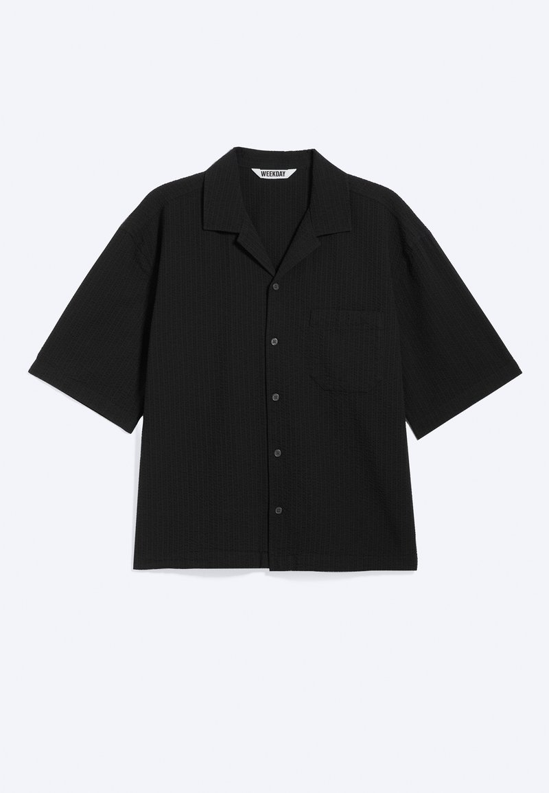 Camisa negra de manga corta con botones, cuello campestre y bolsillo en el pecho, colocada plana sobre un fondo claro.