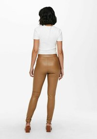 Bílý žebrovaný top s krátkým rukávem v kombinaci s těsnými hnědými kalhotami z umělé kůže. Modelka má na sobě hnědé sandály na blokovém podpatku. Jednoduchý a elegantní design.