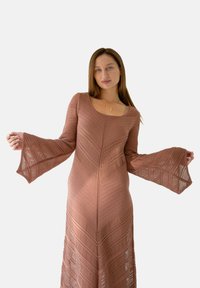 Długa, dopasowana sukienka z miękkiej, przykurzonej różowej dzianiny z rozkloszowanymi rękawami. Oferuje fakturowane wzory w zygzak i dekolt w serek.