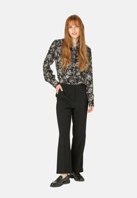 Blusa negra con estampado floral y mangas abullonadas, combinada con pantalones negros ajustados. Los accesorios incluyen unos zapatos negros tipo mocasín.