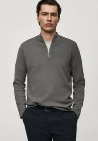 Grå texturerad polotröja med halvdragkeps, bärs över en vit skjorta. Har långa ärmar och en figurnära design.