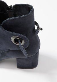 Botín de piel azul marino con punta redonda, acentos metálicos redondos y cremallera lateral; cuenta con un tacón grueso y una textura suave.