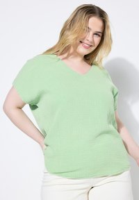 Top verde, a maniche corte con scollatura a V, realizzato in tessuto strutturato con un motivo a griglia; vestibilità ampia con orlo curvo.