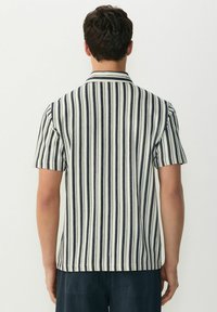 Camisa de manga corta en rayas verticales crema y azul marino, con cuello y tejido texturizado. Vista trasera mostrada.