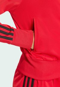 Röd sportjacka med svarta randiga detaljer, en zipficka på sidan samt ribbade muddar och fåll för en åtsittande passform.