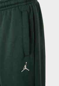 Tmavohned�é tepláky s elastickým pásom, bočnými vreckami a bielym logom Jumpman na ľavom stehne. Mäkká textúra látky.