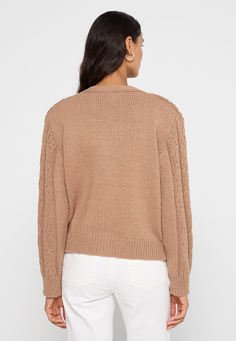 Kuscheliger beiger Pullover mit strukturiertem Strickmuster und geflochtenen Details an den Ärmeln. Mit Rundhalsausschnitt und geripptem Saum.