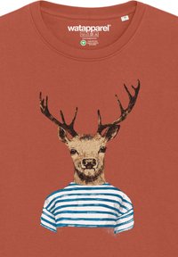 T-shirt couleur rouille avec un graphique d'un cerf portant des bois, vêtu d'une chemise rayée bleue et blanche. Texture douce, design à col rond.