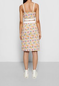 Vaaleanpunainen lyhyt toppi ja siihen sopiva polvimittainen hame, jossa on monivärinen ruutukuosi. Yhdistetty valkoisiin korkeakantaisiin tennareihin.