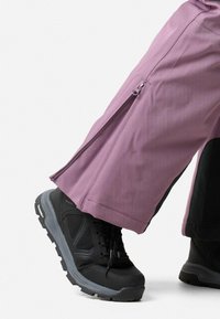 Paarse, lichte broek met ritsopeningen aan de zijkanten, gecombineerd met stevige zwarte schoenen met een gestructureerde zool en grijze accenten.