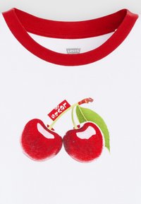 Balta medvilninė marškinėliai su raudonu ribbiniu apvaliu kaklu, ant kurio yra grafika su dviem blizgančiomis raudonomis vyšniomis ir mažas raudonas žymeklis su tekstu.
