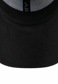 Écusson noir d'une casquette avec des coutures visibles et une doublure intérieure douce, montrant un texte de label partiel à l'intérieur du chapeau.