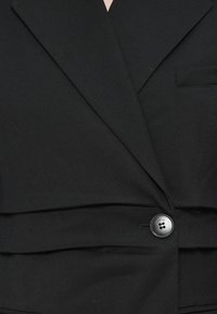 Svart blazer med en skreddersydd design, notched lapel, knapplukking og en enkelt brystlomme, laget av glatt stoff.