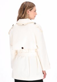 Krém színű ballonkabát övvel a deréknál, nagy gombokkal és hátul egy redővel. Hosszú ujjú és sima tapintású.
