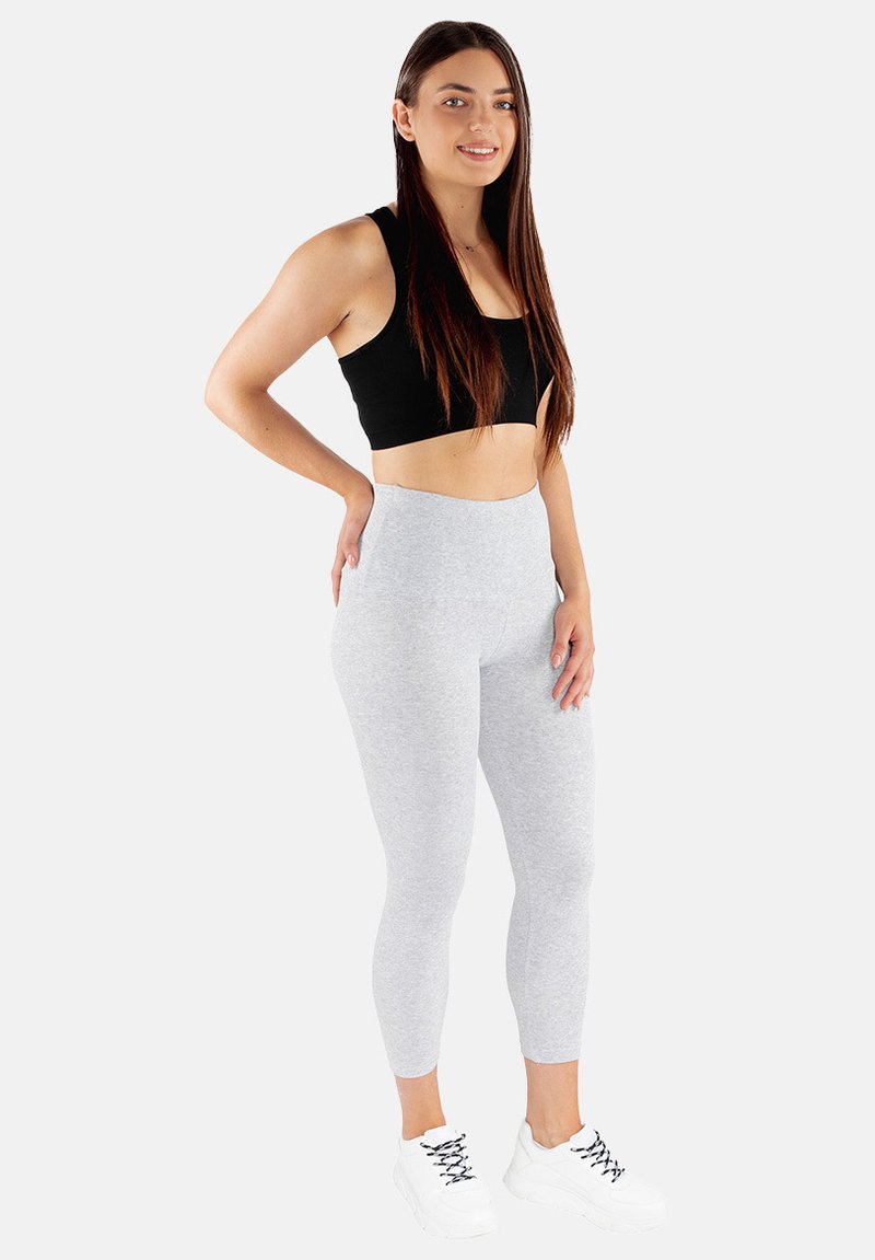 Szare legginsy z wysokim stanem, zestawione z czarnym topem krótkim. Model nosi białe buty sportowe z czarnymi sznurowadłami. Gładka faktura materiału.