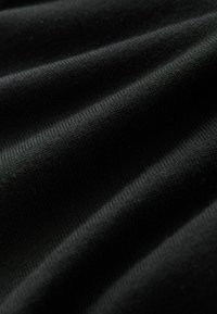 Gros plan d'un tissu noir côtelé montrant une texture douce et de légers plis sous un éclairage naturel.