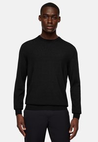 Black knitted sweater with a round neckline, long sleeves, ribbed cuffs, and a textured finish, paired with dark pants.