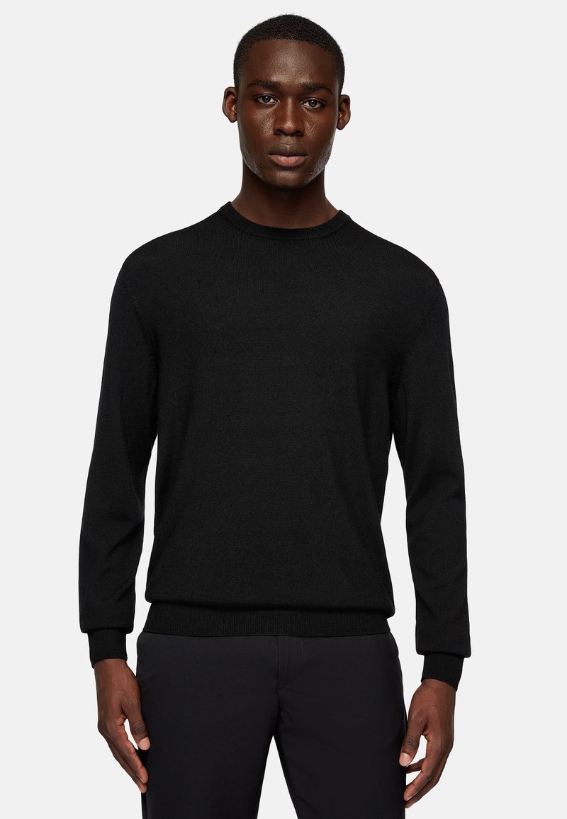 Black knitted sweater with a round neckline, long sleeves, ribbed cuffs, and a textured finish, paired with dark pants.