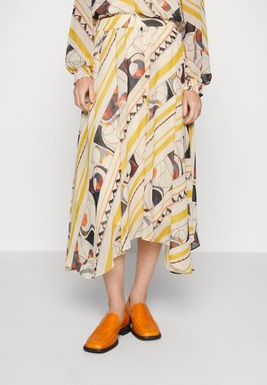 Falda larga y fluida con patrones geométricos multicolores y rayas amarillas; hecha de un tejido ligero. Se lleva con zapatos de lona de color naranja brillante.