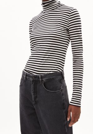 Henkilö, jolla on päällään mustavalkoinen vaakaraitainen poolopaita ja korkeavyötäröiset haalistuneet mustat farkut, seisoo yhdellä kädellä rentona.