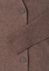 Hnědý pletený kardigan s texturovaným povrchem, vybavený žebrovanými manžetami a zapínáním na dva tmavé knoflíky vpředu.