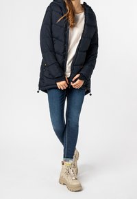 Námořnická prošívaná bunda s kapucí, žebrovanými manžetami a zipovými kapsami. Nosí se přes světlou košili a v kombinaci s modrými džíny a světlými botami.