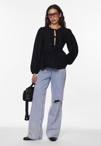 Svart peplumblus med rund halsringning och två framknutar, ihopparad med ljusblå högmidjade jeans med ett trasigt högra ben, och en svart väska.