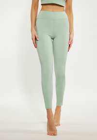 Világoszöld leggings, rugalmas anyagból készült, magas derékkal, sima textúrával és testhezálló kialakítással, bokáig érő hosszal.