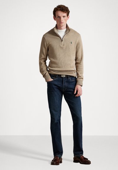 Beige zip-hals sweater med ribbede manchetter, parret med mørkeblå jeans. Brune loafers fuldender outfittet. Enkel, klassisk design.