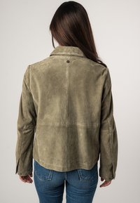 Giacca in suede verde oliva con una texture liscia, colletto a scollo, e dettagli con bottoni, caratterizzata da un fit rilassato e cuciture sul retro.