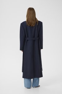 Long navy coat in a wool blend, featuring a belted waist, wide sleeves, and a straight cut. Paired with light blue wide-leg jeans.