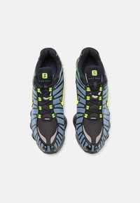 Nike Shox -lenkkitossut, joissa musta ja sininen verkkomateriaali, neonvihreät yksityiskohdat, teksturoitu pohja ja pehmustettu kaulus mukavuutta varten.