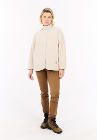 Beige fleece jack met grote zakken, voor knopen en ronde kraag, gecombineerd met bruine slim fit broek en bruine wandelschoenen.
