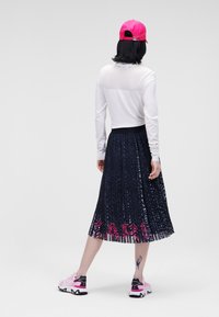 Haut blanc à manches longues avec dos en maille, jupe plissée bleu marine avec motif rose et bleu, casquette rose et chaussures de sport roses avec accents noirs.