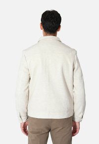 Giacca in misto lana color beige chiaro con collo a camicia, dettagli con bottoni e una finitura leggermente testurizzata. Design semplice, adatta per essere indossata a strati.