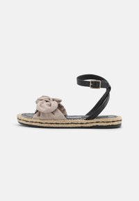 Mustat espadrillesandals, joissa on nuden värinen kankainen rusetti. Varustettu punotulla juuttipohjalla, säädettävällä nilkkahihnalla ja kumipohjalla.