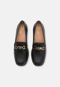Melnas ādas loafers ar noapaļotu purngalu, ar zeltītām sirds formas detaļām un brūnu iekšzoli, uz kuras ir iegravēts "LOVE MOSCHINO."