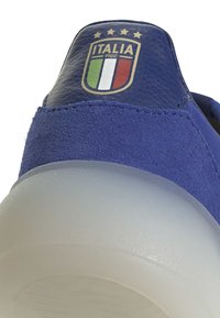 Modré semišové tenisky s texturovanou patou, zdobené embosovaným logem ITALIA FIGC a čtyřmi hvězdami. Průhledná gumová podrážka.