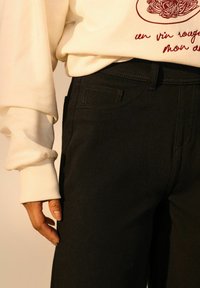 Pantaloni din denim negri, cu o croială clasică, având buzunare laterale, detalii de cusătură subtile și un material texturat. Combinați cu un Hanorac alb.
