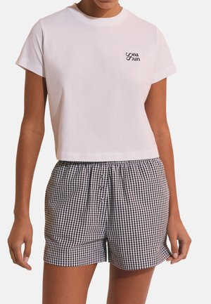 Donna che indossa una maglietta corta bianca con la scritta "Sea Sun" e pantaloncini a vita alta a quadri in bianco e nero con bottoni.